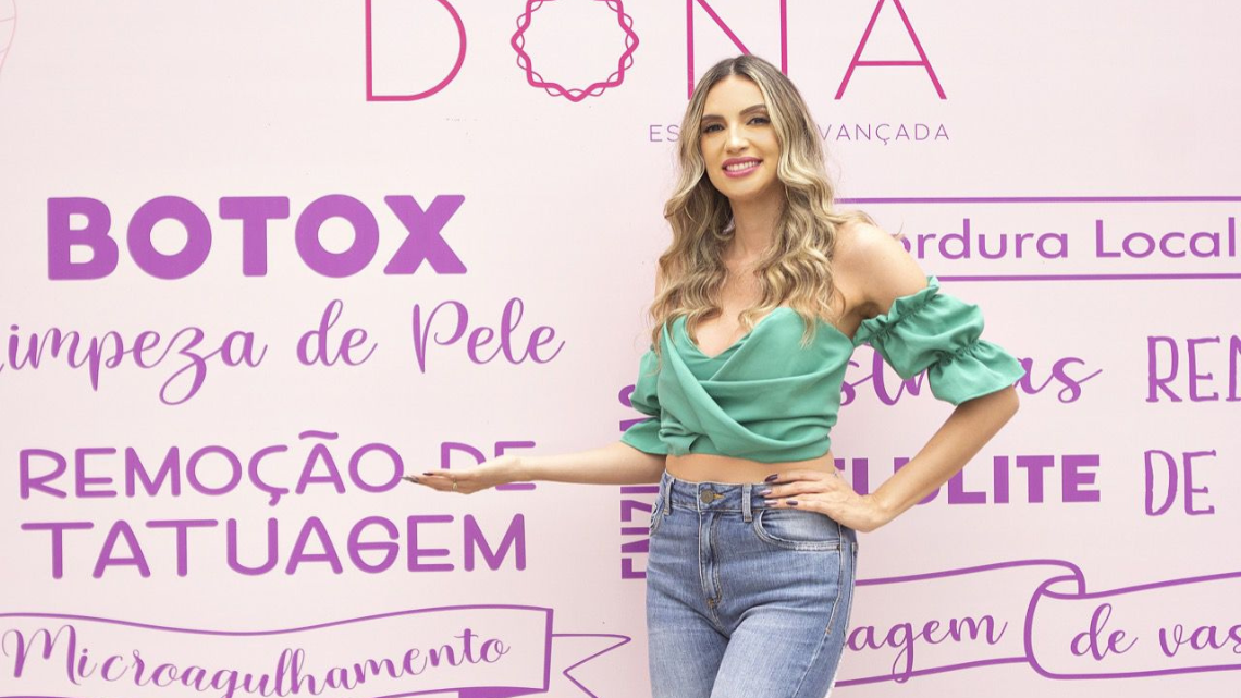 Dra. Hellenn em frente ao painel de tratamentos da Clínica Dona